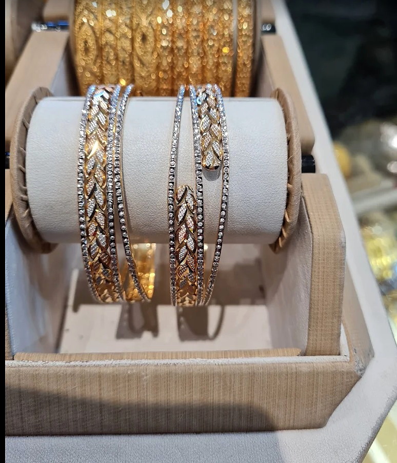 Diamond-cut gold and white gold bangles displayed on a cream velvet roll at Ramzan Jewellers