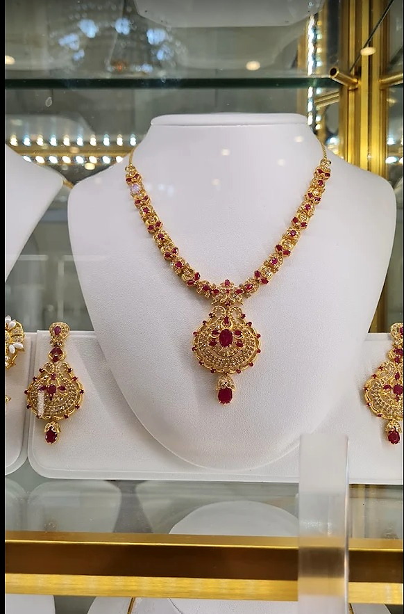 Gold necklace and earring set with red stones on a display bust at Ramzan Jewellers