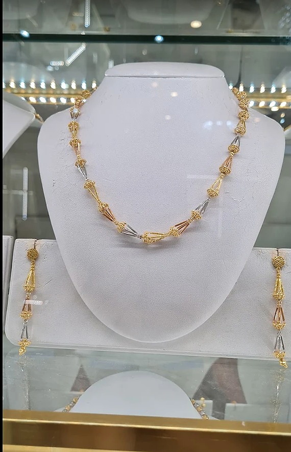 Two-tone gold beaded necklace with matching drop earrings on a display bust